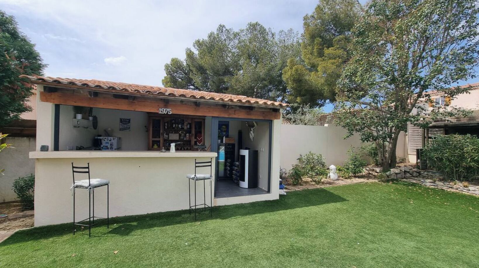 A small outdoor bar with a tiled roof, two bar stools, and a counter.