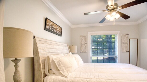 Une chambre à coucher avec un grand lit, une table de chevet en bois, un ventilateur de plafond et une fenêtre avec des stores.