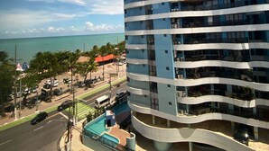 A modern multi-story building with a curved facade, located near a coastal area with visible ocean and palm trees.