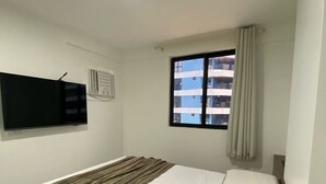 A hotel room with a bed, a window with curtains, a flat-screen TV mounted on the wall, and a ceiling light.