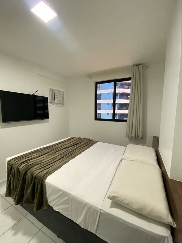 A hotel room with a bed, a window with curtains, a flat-screen TV mounted on the wall, and a ceiling light. - Edificio Neo Apto 602-Mandi H (Maceio)