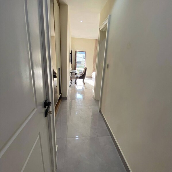 A hallway with a flat floor, doors on the left, and a window at the end.