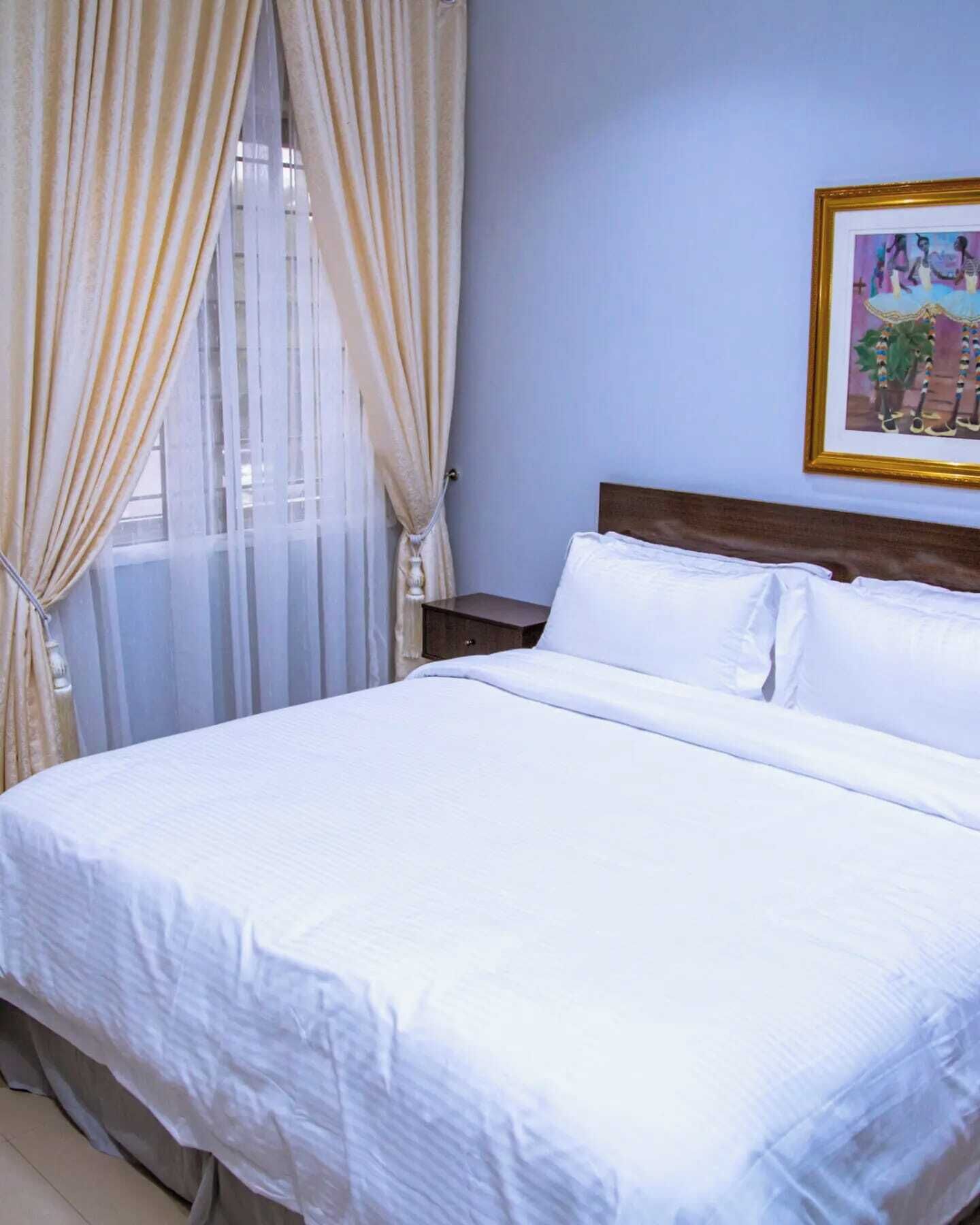 A neatly made bed in a room with light blue walls, a wooden headboard, and a framed picture on the wall.
