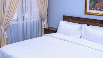 A neatly made bed in a room with light blue walls, a wooden headboard, and a framed picture on the wall.