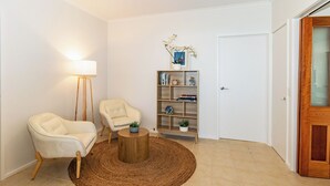 A living room with two white armchairs, a round wooden coffee table, a floor lamp, a bookshelf, and a door with a glass panel.