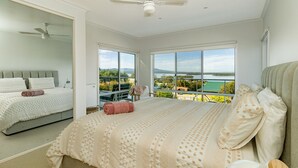 A bedroom with a large bed, a second bed, a view of the outdoors, and a ceiling fan.