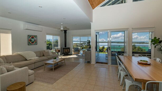 A modern living room with a sofa, coffee table, and a fireplace. There is a balcony with a view of the sea.