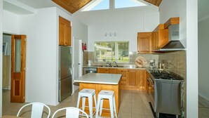A modern kitchen with wooden cabinets, a stainless steel refrigerator, a gas stove, and a large window.