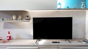 Ein modernes Wohnzimmer mit einem an der Wand montierten Flachbildfernseher, Holzschränken darunter und dekorativen Gegenständen auf Regalen.