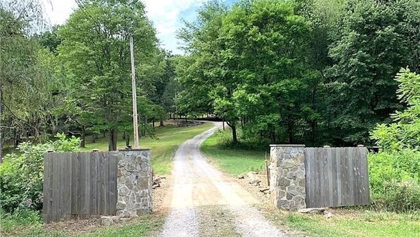 A gravel driveway leading to a gated area with stone walls and wooden gates, surrounded by lush greenery and trees. - 10acre Serene Retreat W/ ⭐️⭐️⭐️⭐️⭐️Private Chef Availability!!  (Mars)