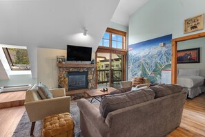A modern living room with a stone fireplace, a flat-screen TV, and a large window overlooking a deck. - Es8630-1 (Keystone)