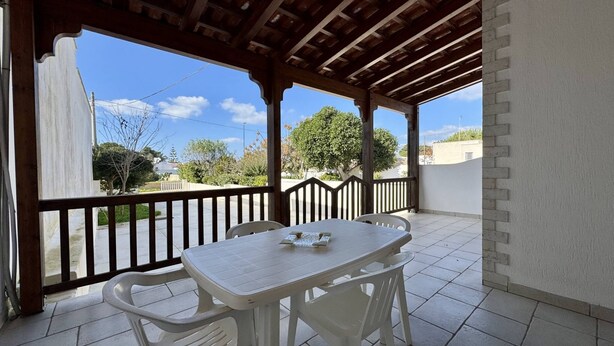 Une terrasse couverte avec une table et des chaises, une balustrade en bois et une vue sur les environs.