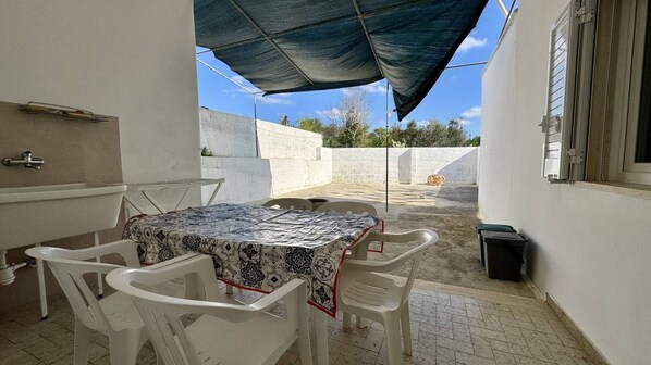 A patio with a table and chairs, a sink, and a window with blinds. - Villetta Marilena Sleeps 7 Torre Suda (Racale)