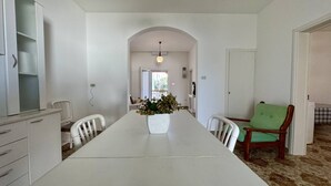 Une salle à manger avec une longue table, des chaises blanches, un vase rempli de fleurs et une chaise verte.
