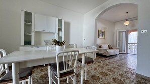 Un coin repas avec une table et des chaises blanches, une cuisine avec des meubles blancs et un salon avec un canapé et un tableau.