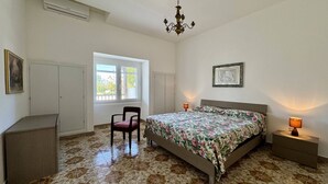 Une chambre à coucher avec un lit, une chaise, un bureau, une fenêtre et un lustre.