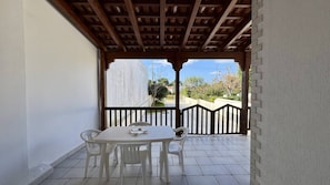 Un patio couvert avec une table et des chaises, une vue sur la rue et une pergola en bois.