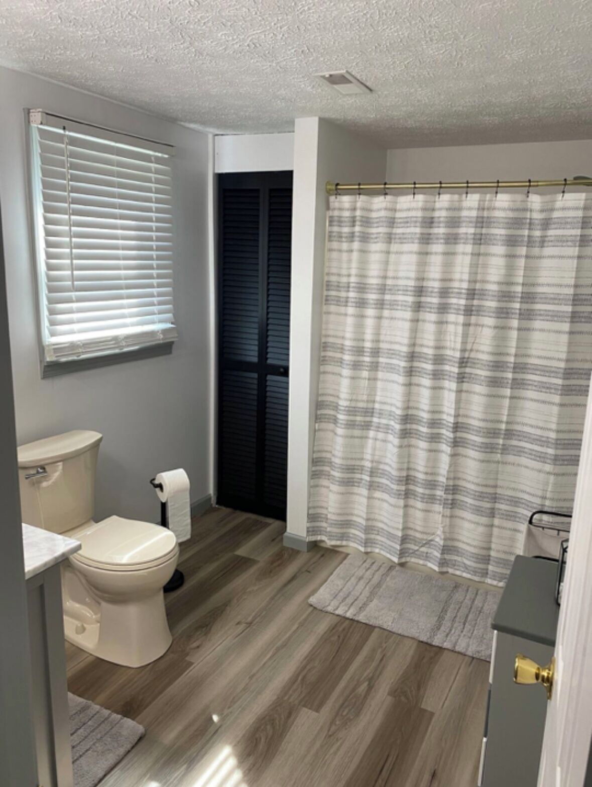 A bathroom with a toilet, a shower curtain, and a window with blinds.