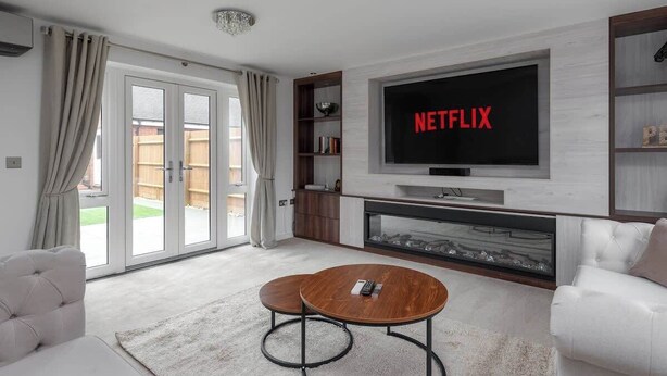 Ein modernes Wohnzimmer mit einem Flachbildfernseher, der "NETFLIX" anzeigt, einem Kamin, einer Couch und einem Couchtisch.