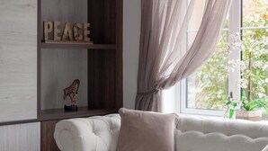 Ein Wohnzimmer mit einem weißen Sofa, einem Holzregal mit Dekorationen, einem Fenster mit durchscheinenden Vorhängen und einem Blumentopf.