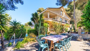 A house with a patio area featuring a table and chairs, surrounded by various plants and trees. - Private Pool & Stunning Mountain Views (Tarragona)