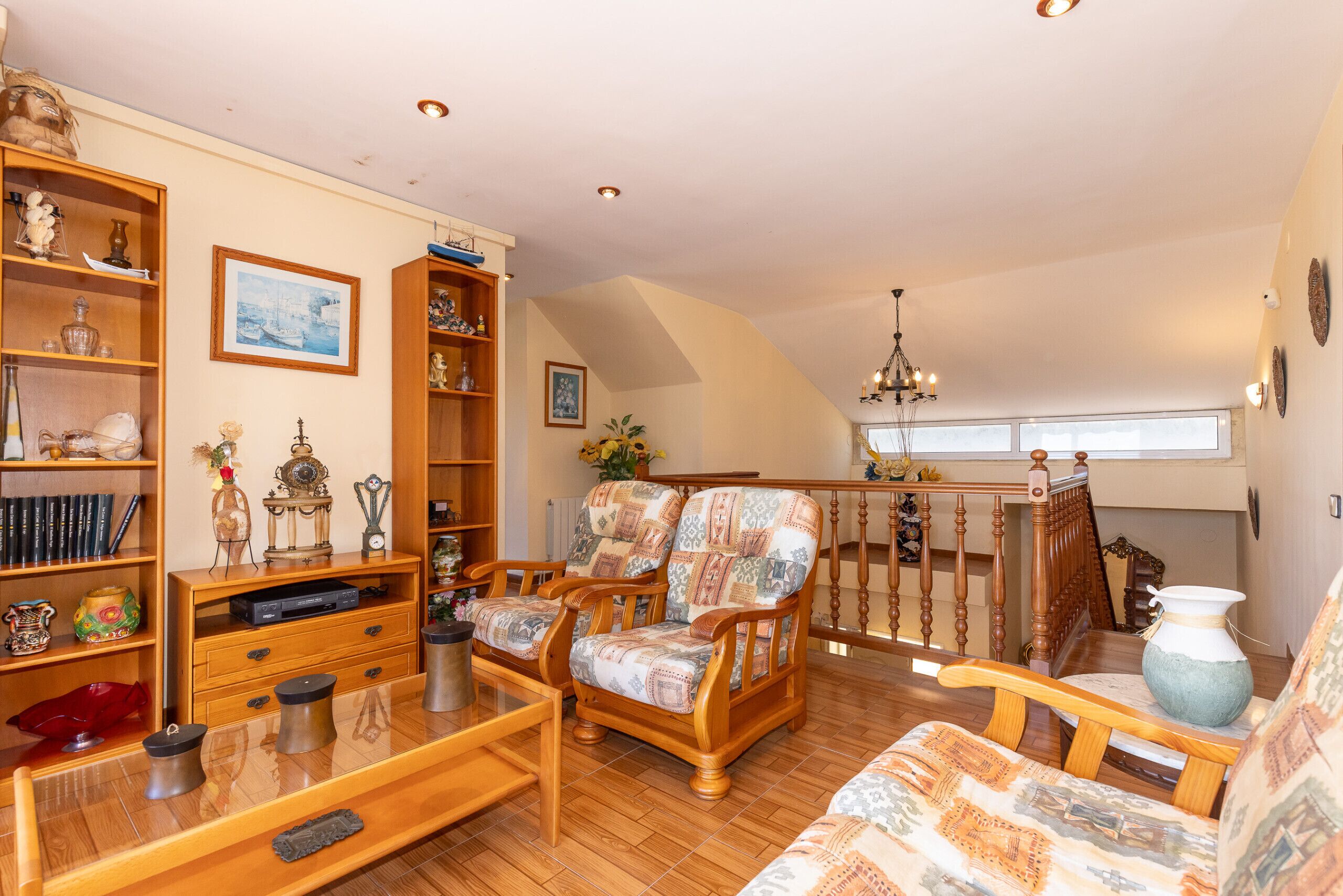 A spacious living room with wooden furniture, a bookshelf, and a staircase leading to an upper level.