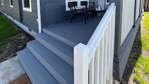Una casa residencial con un porche cubierto, un pequeño espacio al aire libre con dos sillas y un conjunto de escaleras que conducen a la entrada.