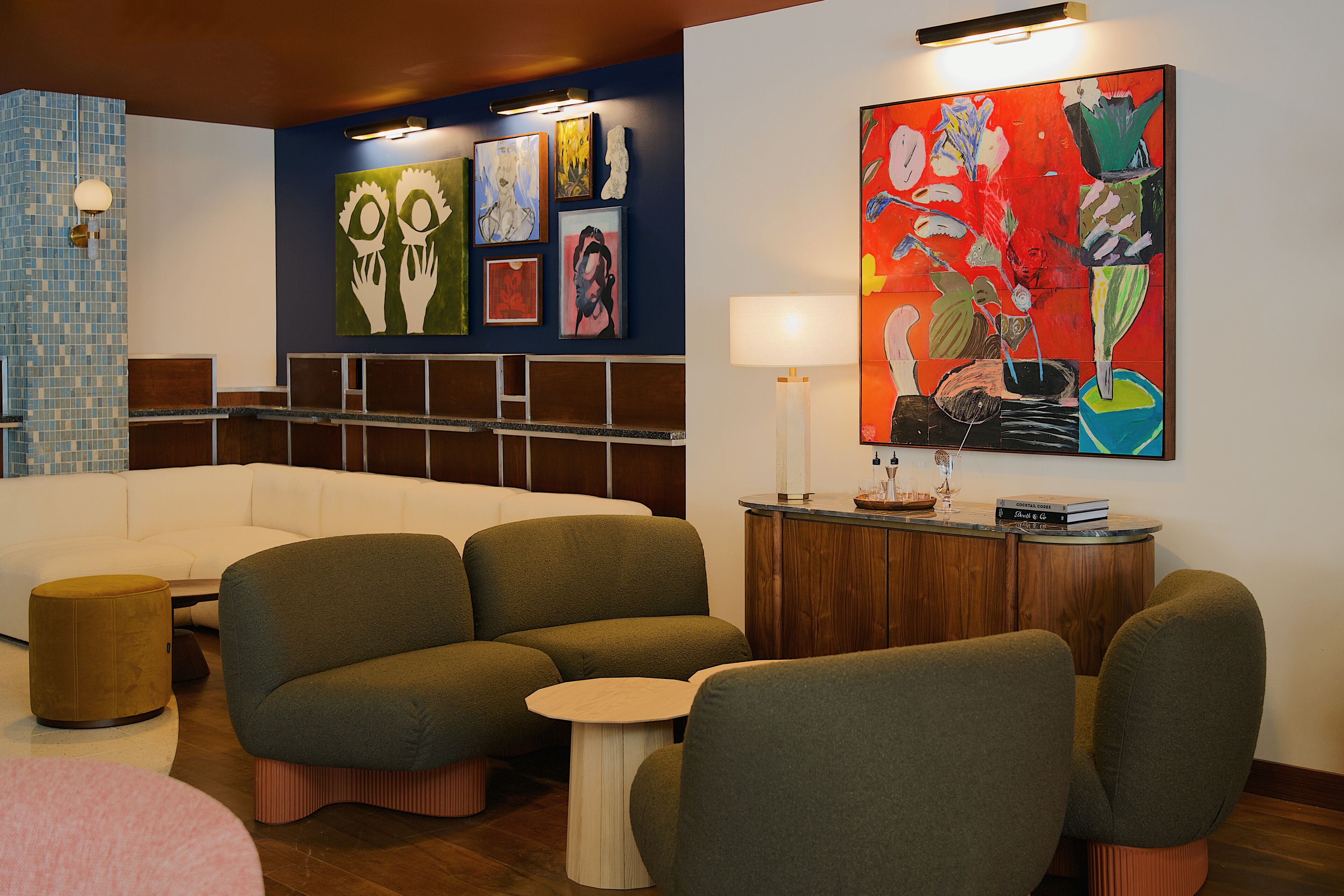 A modern lounge area with a sofa, armchairs, a small table, and a cabinet with books and a lamp.