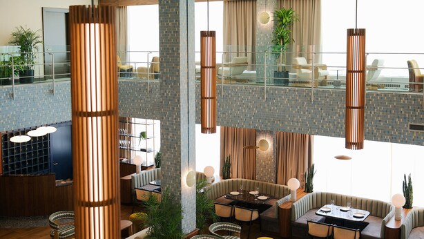 Een ruime hotellobby met een hoge plafond, meerdere zithoeken en een glazen balustrade met uitzicht op het terras.