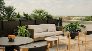 Een terras op het dak, met een bank, twee ronde tafels en houten stoelen.