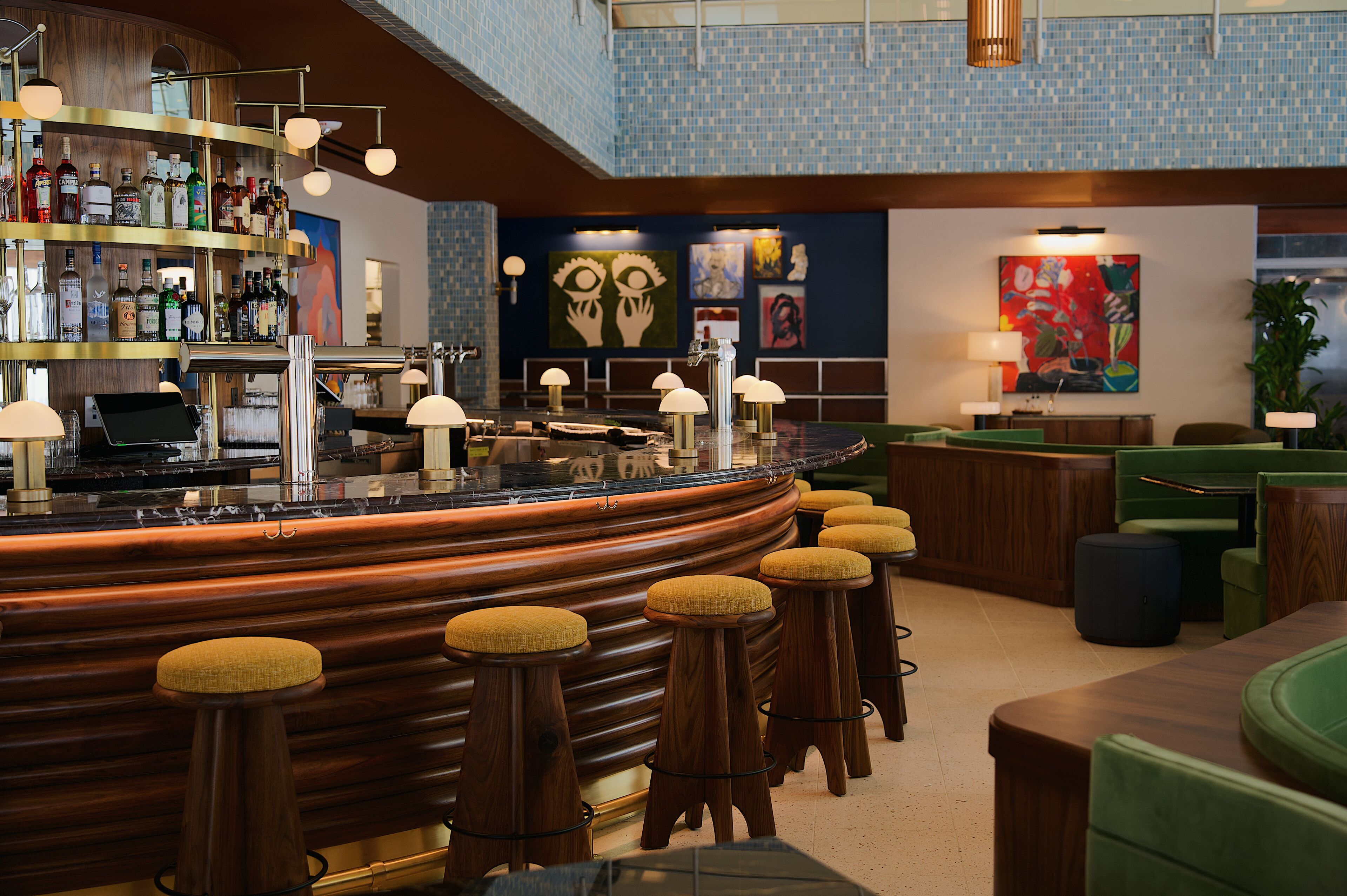 A bar area with stools, a counter with a cash register, and a variety of bottles.