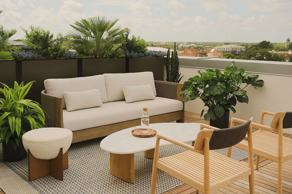 A rooftop terrace with a sofa, chairs, a small table, and potted plants.