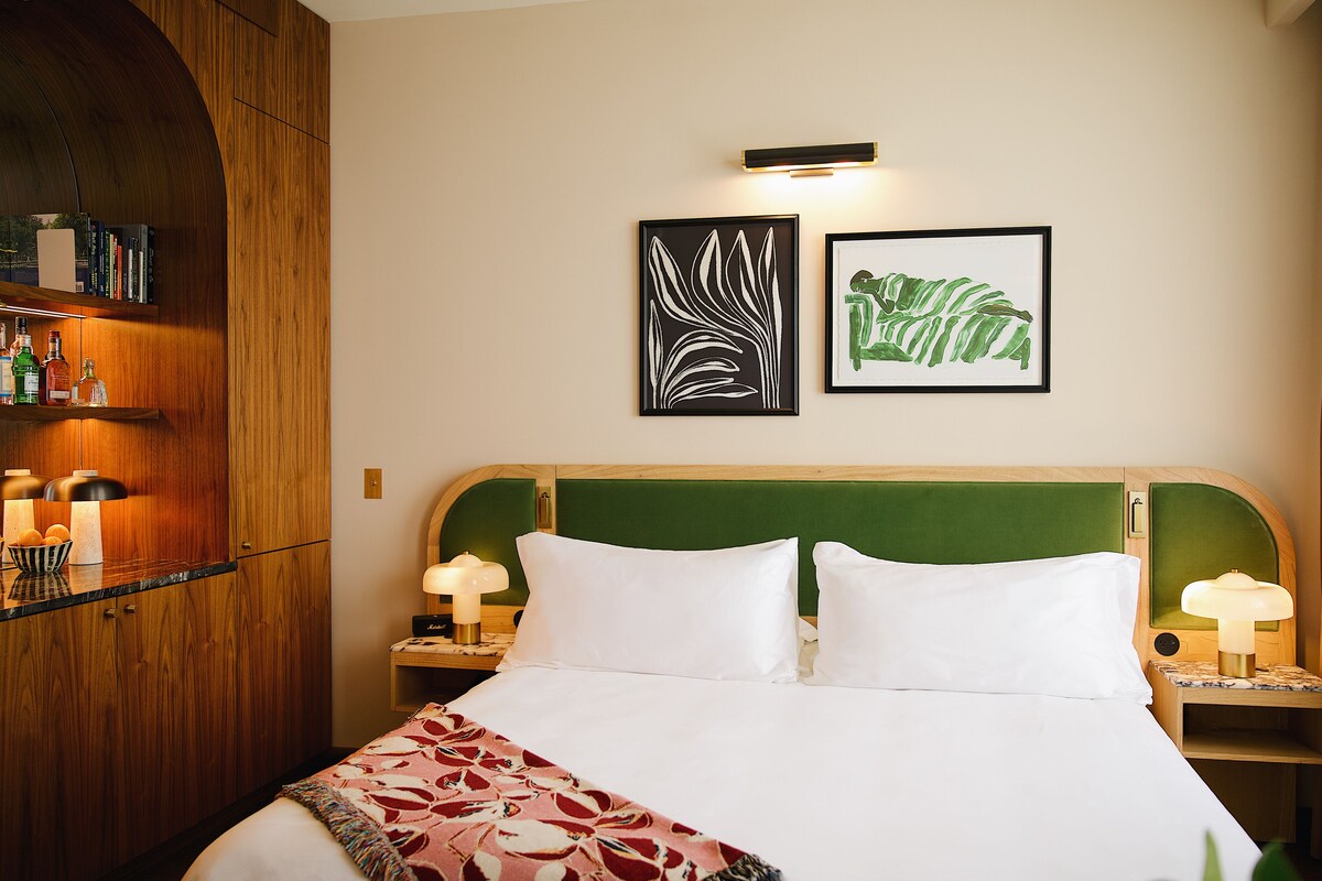 A neatly made bed with white linens, a green headboard, and two bedside lamps. There are framed artworks on the wall above the bed.
