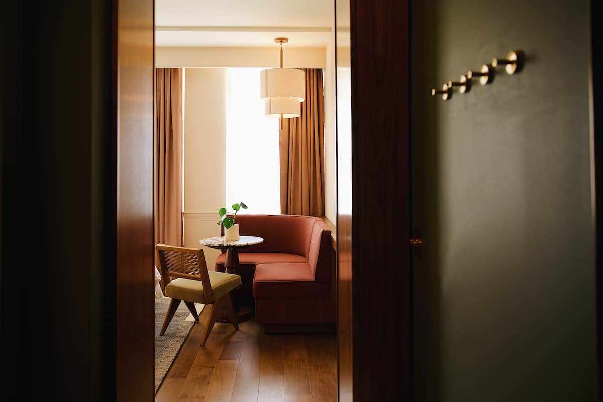 A hotel room with a wooden floor, a red sofa, a small round table with a plant, and a chair.