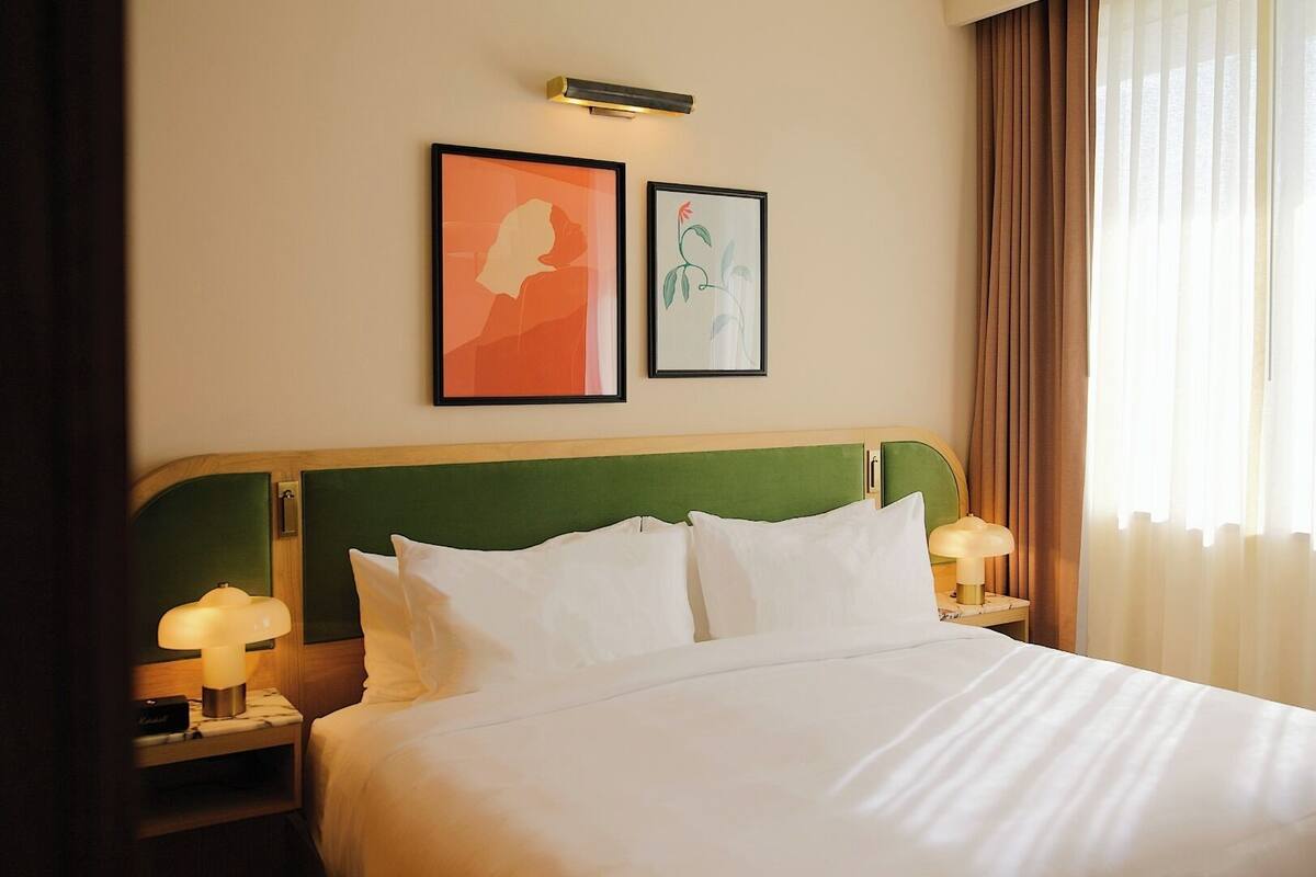 A hotel room with a large bed, two bedside lamps, and two framed artworks on the wall.
