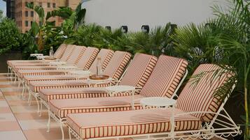 A row of striped lounge chairs with white metal frames and cushions, arranged on a tiled patio with palm plants in the background.