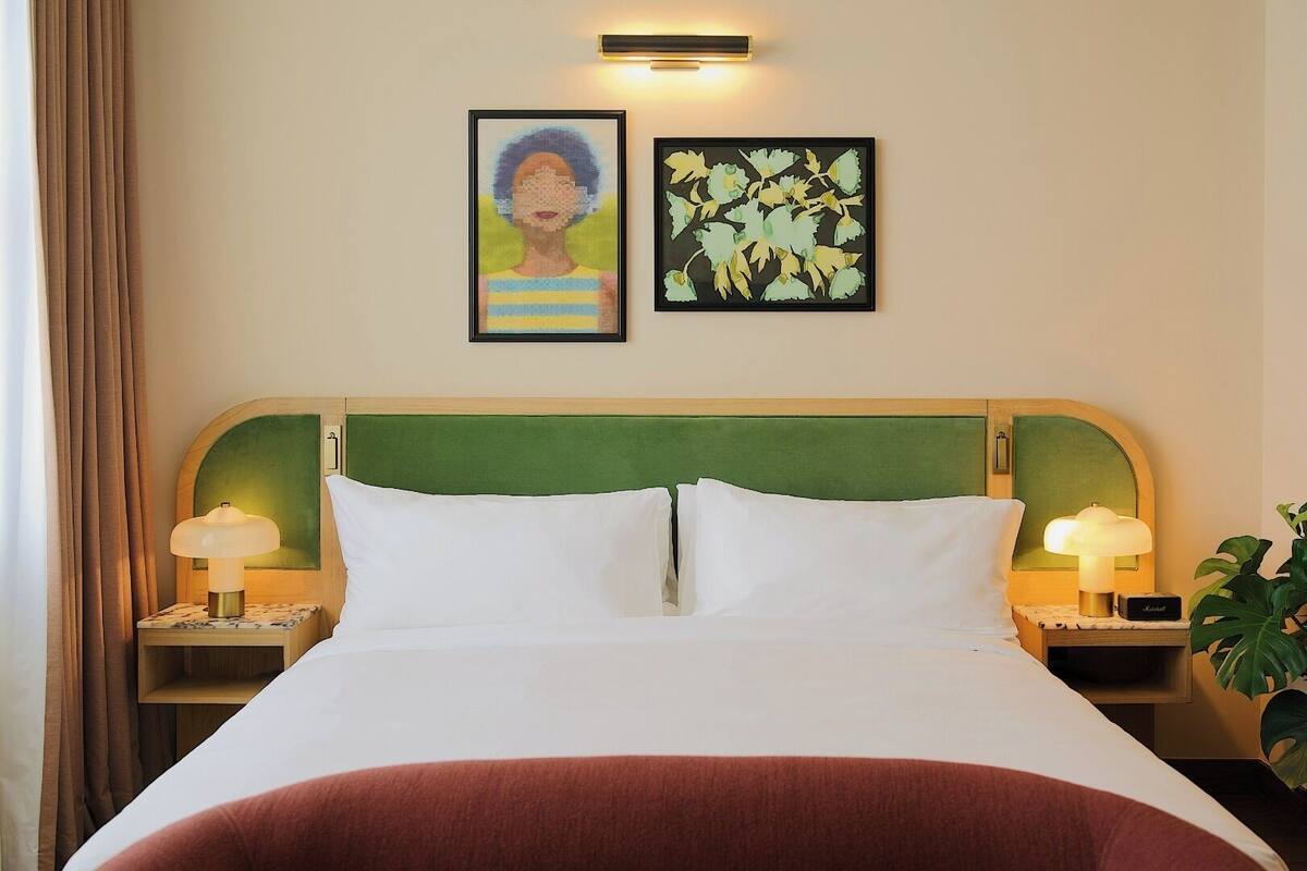 A hotel room with a bed, two nightstands, two lamps, a green headboard, and two framed artworks on the wall.