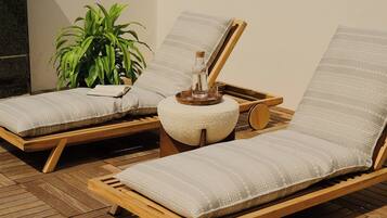 Dos sillones de madera con cojines a rayas, una mesita redonda con una botella y un vaso, y una planta en maceta.