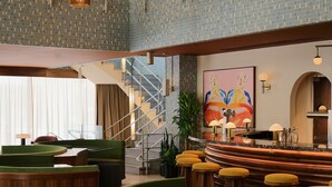 Een hotellobby met een gebogen bar, zithoek, trap en een groot abstract schilderij.