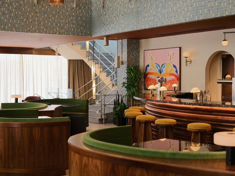 Un hall d’hôtel doté d’un bar incurvé, d’un espace salon, d’un escalier et d’un grand tableau abstrait.