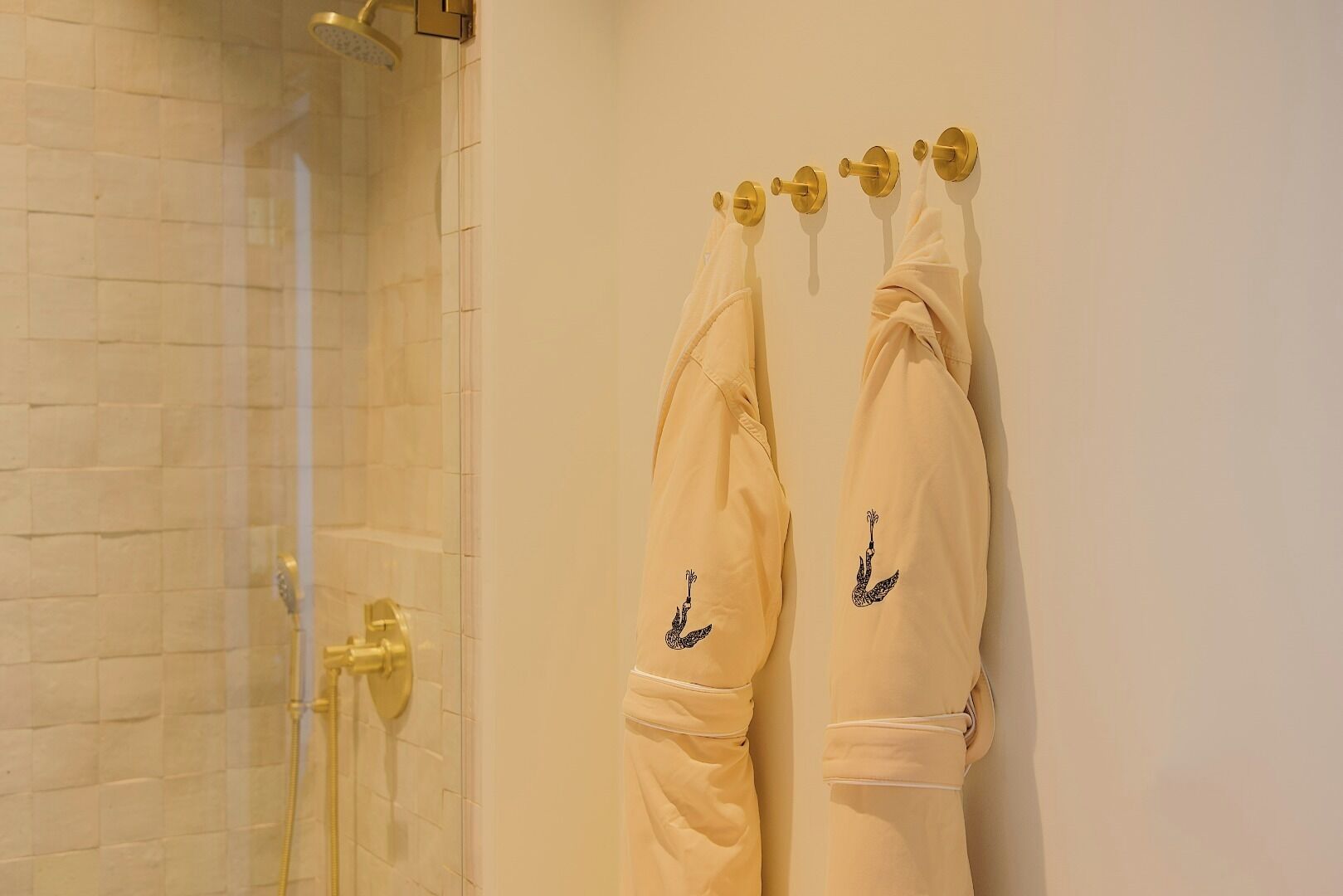 Une salle de bain avec une douche à parois de verre, un mur recouvert de carreaux blancs et deux serviettes suspendues à un porte-serviettes.
