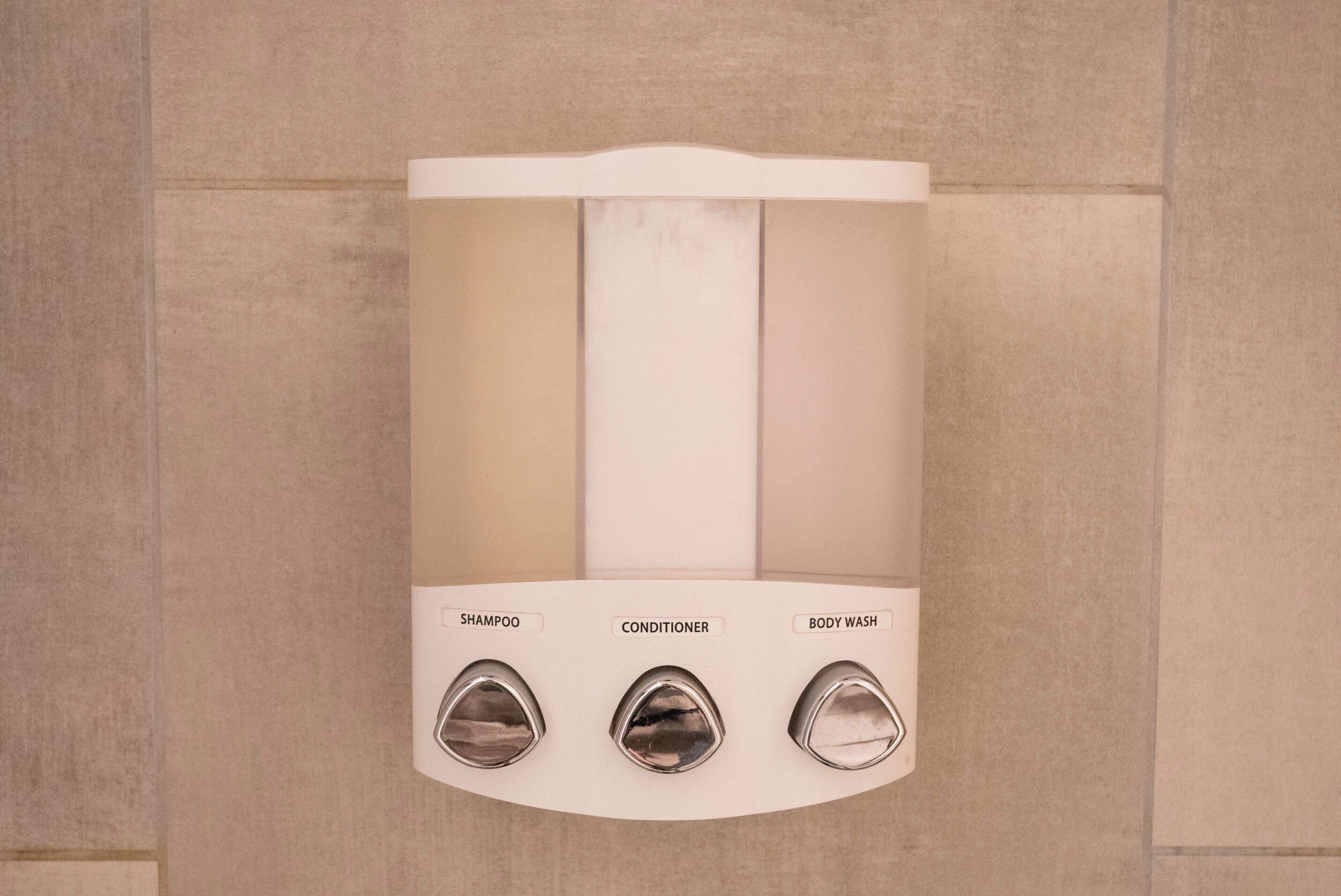 Ducha empotrada con tres mandos etiquetados como 'champú', 'acondicionador' y 'gel de ducha'.