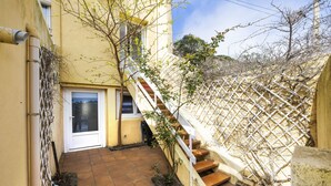 A narrow courtyard with a tiled floor, a white door, a wooden staircase, and a white lattice fence. - La Belle Escapade - Climatisée, aperçu mer (Port-Vendres)