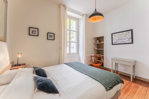 A bedroom with a bed, a desk, a chair, a map on the wall, and a window.