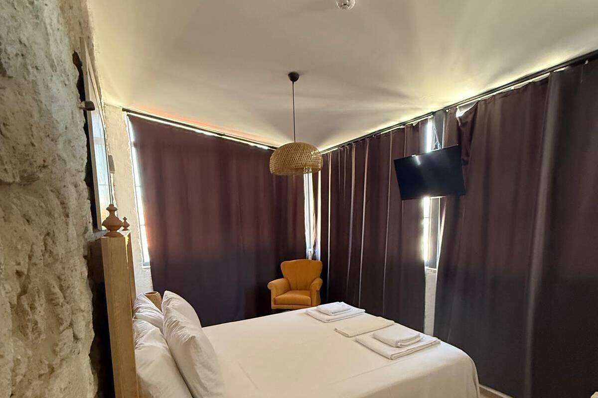 Un dormitorio con una cama grande, televisión, una pequeña silla y una lámpara colgante.