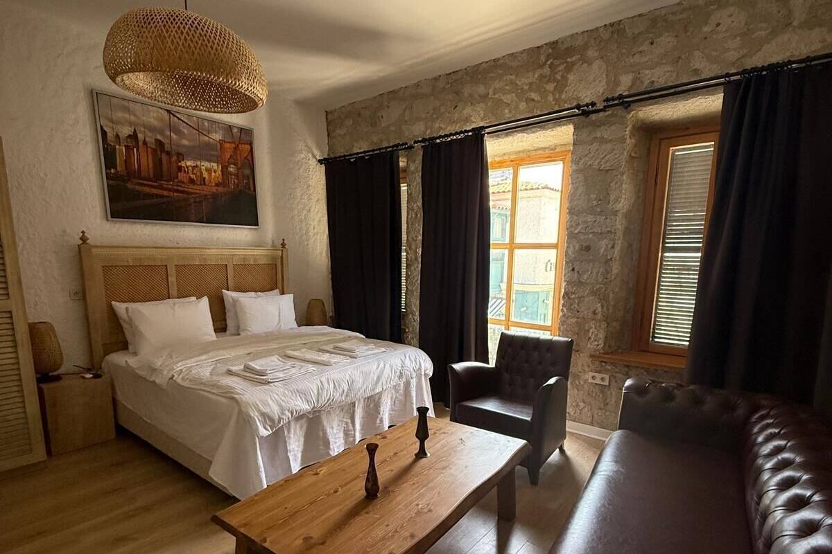 Un dormitorio con cama, mesa de madera, sofá de cuero, una silla y una lámpara colgante.