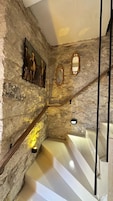 Una escalera con paredes de piedra, un cuadro de caballos y dos espejos ornamentados.