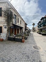 Una calle adoquinada flanqueada por edificios históricos, mesas al aire libre y plantas en macetas.