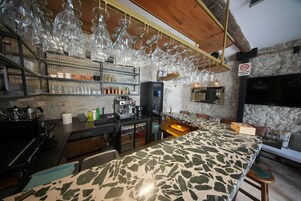 Zona de bar con una barra larga, cristalería colgante, estantes con botellas y una máquina de café.