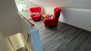 A spacious attic room with a sloped ceiling, two red armchairs, a small wooden table, and a window with a view of greenery. - Vidi Apartmens: By the stream (Bad Überkingen)